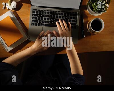 Vue aérienne d'une femme dactylographiant à la main sur un ordinateur portable en bois table avec papeterie et pot de plantes Banque D'Images