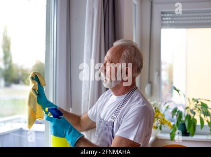 Portrait d'un homme âgé qui nettoie les fenêtres à la maison. Concept de nettoyage de ressort Banque D'Images