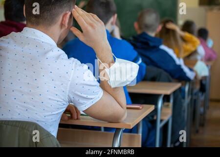 Vue arrière des enfants assis au bureau de l'école avec masques de protection sur les mains Banque D'Images
