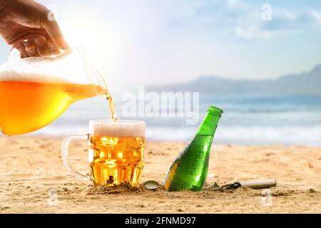 Concept de refroidissement sur la plage avec une main d'homme qui verse un verre de bière dans une tasse. Vue de face. Banque D'Images