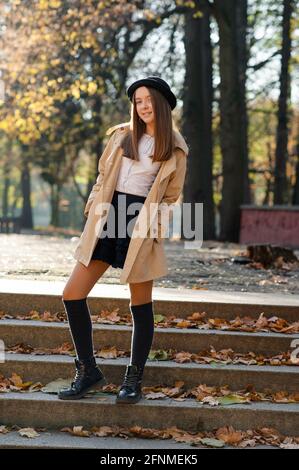 Tenue décontractée. Belle jeune fille posant sur les marches dans un parc d'automne souriant à la caméra de mise au point douce Banque D'Images