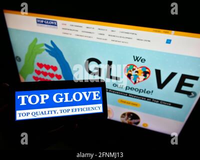 Personne tenant un smartphone avec le logo de la société malaisienne Top Glove Corporation Berhad à l'écran devant le site Web. Mise au point sur l'affichage du téléphone. Banque D'Images