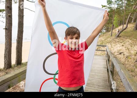 Riga, Lettonie, mai 16. 2021. Garçon avec drapeau des Jeux Olympiques. Symbole de cinq anneaux Banque D'Images