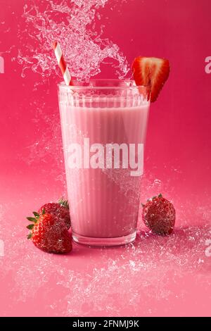 Milkshake aux fraises éclaboussant dans le verre sur fond rose Banque D'Images