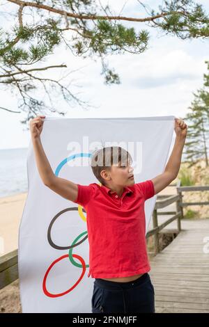 Riga, Lettonie, mai 16. 2021. Garçon avec drapeau des Jeux Olympiques. Symbole de cinq anneaux Banque D'Images