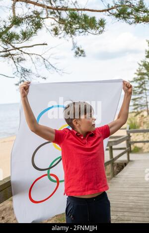 Riga, Lettonie, mai 16. 2021. Garçon avec drapeau des Jeux Olympiques. Symbole de cinq anneaux Banque D'Images