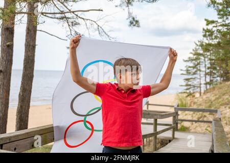 Riga, Lettonie, mai 16. 2021. Garçon avec drapeau des Jeux Olympiques. Symbole de cinq anneaux Banque D'Images