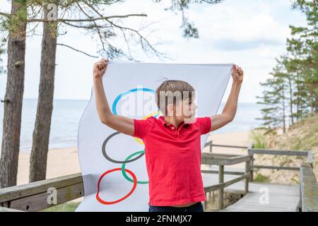 Riga, Lettonie, mai 16. 2021. Garçon avec drapeau des Jeux Olympiques. Symbole de cinq anneaux Banque D'Images