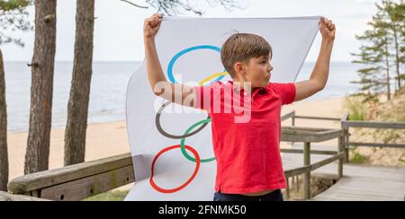 Riga, Lettonie, mai 16. 2021. Garçon avec drapeau des Jeux Olympiques. Symbole de cinq anneaux Banque D'Images