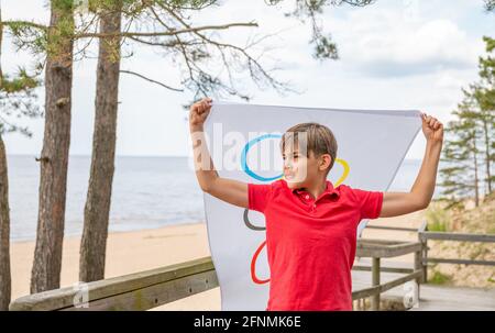 Riga, Lettonie, mai 16. 2021. Garçon avec drapeau des Jeux Olympiques. Symbole de cinq anneaux Banque D'Images