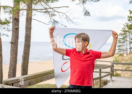 Riga, Lettonie, mai 16. 2021. Garçon avec drapeau des Jeux Olympiques. Symbole de cinq anneaux Banque D'Images