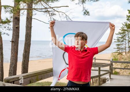 Riga, Lettonie, mai 16. 2021. Garçon avec drapeau des Jeux Olympiques. Symbole de cinq anneaux Banque D'Images