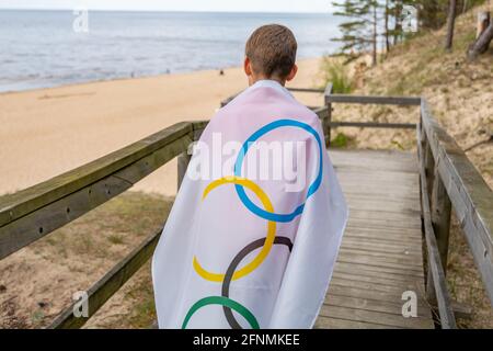 Riga, Lettonie, mai 16. 2021. Garçon avec drapeau des Jeux Olympiques. Symbole de cinq anneaux Banque D'Images