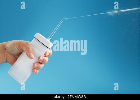 Irrigateur en main pour nettoyer la bouche avec un jet d'eau sur fond bleu. Un appareil mobile pour se brosser les dents et un sourire blanc neige Banque D'Images
