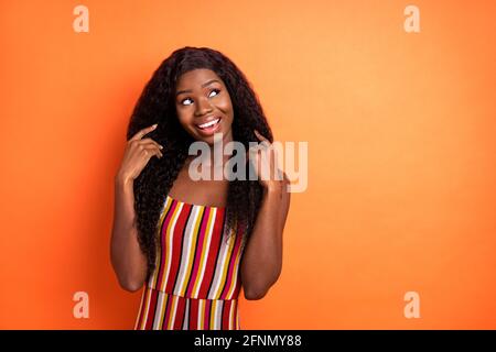 Photo de peau sombre rêveuse jeune fille gaie regarder vide espace été isolé sur fond de couleur orange Banque D'Images