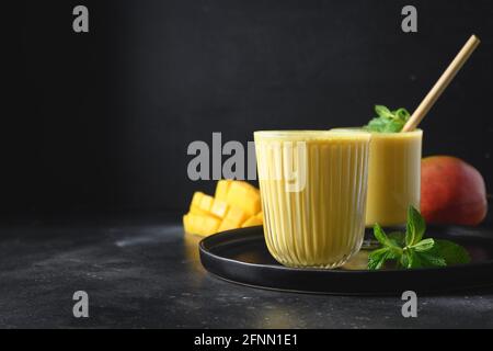Deux lassi de mangue dans des verres sur fond noir avec espace de copie. Boisson fraîche ayurvédique saine indienne à la mangue. Lassi frais à base de yaourt, eau, Banque D'Images
