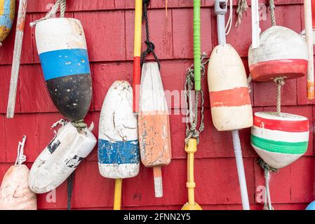 Gros plan de vieilles bouées de pêche colorées accrochées sur le mur extérieur en bois rouge d'une cabane de pêche dans un port Banque D'Images