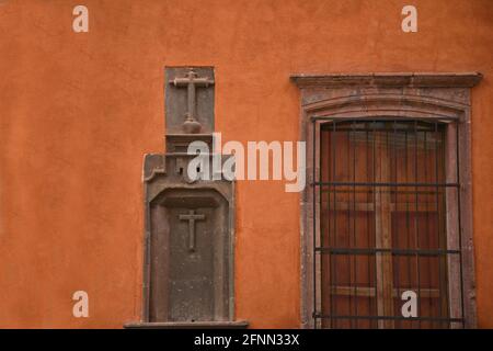 Façade de l'église gothique avec fenêtres en pierre et symboles religieux en céramique sur un mur en stuc rouge vénitien à San Miguel de Allende, Mexique. Banque D'Images