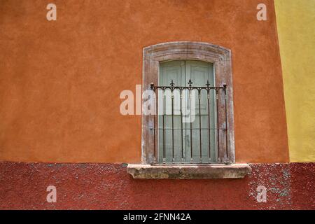 Maison coloniale fenêtre avec bordure en pierre et balcon avec balustrade en fer fait à la main sur un mur en stuc ocre terre cuite à San Miguel de Allende, Mexique. Banque D'Images