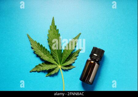 Huile de marijuana et feuille de cannabis. Bouteille de beurre sur fond bleu. Médecine alternative. Chanvre récréation, usage médical, légalisation. Banque D'Images