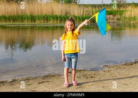 Le drapeau de l'Ukraine flotte entre les mains d'une petite fille sur fond de lac. Jour de l'indépendance de l'Ukraine et jour du drapeau. Banque D'Images