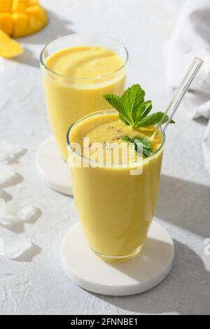 Deux lassi de mangue ou smoothies sur fond gris avec ombre ensoleillée. Boisson fraîche ayurvédique saine indienne à la mangue, au yaourt, à l'eau, aux épices, aux fruits et Banque D'Images