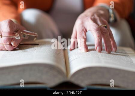 Femme âgée lisant un livre et dans sa main elle tient une paire de lunettes. Banque D'Images