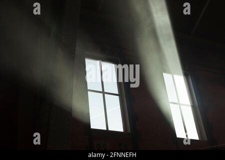 Des rayons de soleil se diffusent à travers les fenêtres d'un grand bâtiment ancien. L'atmosphère intérieure poussiéreuse a créé ces poutres frappantes Banque D'Images