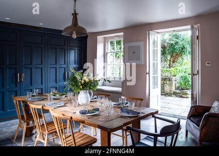 Salle à manger avec armoires dans les rambardes et les murs dans le sol rose et ouvert au jardin, Somerset. Banque D'Images