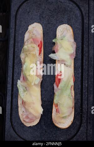 La baguette grillée enduite de beurre et d'huile, de jambon de poulet, de tomate et recouverte de fromage en tranches est cuite jusqu'à ce qu'elle soit dorée sur une pierre de granit placée Banque D'Images