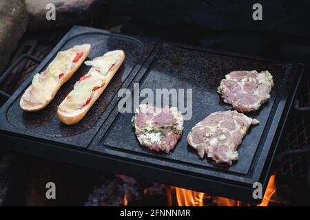 L'homme prépare un collet de porc juteux avec du basilic et des épices barbecue et une baguette avec du fromage de tomate et du jambon sur une plaque de granit chaude. La saison du barbecue a mendier Banque D'Images