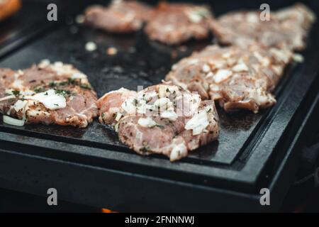 Préparation de morceaux de cou de porc assaisonnés de basilic, sel, huile d'olive, poivre, oignon et ail sur une plaque de granit chaud qui reçoit la chaleur d'un ouvert f Banque D'Images