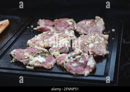 L'homme utilise une louche en acier pour tourner un col de porc chargé avec du basilic, du sel, du poivre et de l'huile d'un côté à l'autre. Barbecue sur un sapin extérieur féroce Banque D'Images