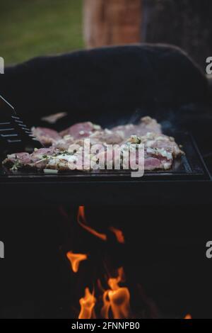 L'homme utilise une louche en acier pour tourner un col de porc chargé avec du basilic, du sel, du poivre et de l'huile d'un côté à l'autre. Barbecue sur un sapin extérieur féroce Banque D'Images