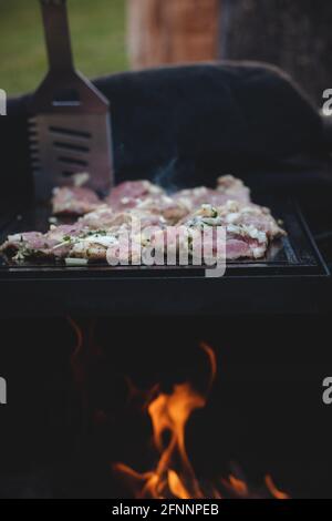 L'homme utilise une louche en acier pour tourner un col de porc chargé avec du basilic, du sel, du poivre et de l'huile d'un côté à l'autre. Barbecue sur un sapin extérieur féroce Banque D'Images