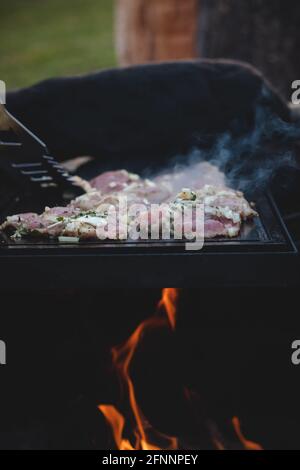 L'homme utilise une louche en acier pour tourner un col de porc chargé avec du basilic, du sel, du poivre et de l'huile d'un côté à l'autre. Barbecue sur un sapin extérieur féroce Banque D'Images