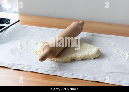 Pâte à caillé crue avec morceaux de fromage cottage, rollpin en bois et farine saupoudrée sur du papier de cuisson sur une nappe en lin sur une table en bois Banque D'Images