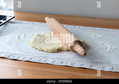 Pâte à caillé crue avec morceaux de fromage cottage, rollpin en bois et farine saupoudrée sur du papier de cuisson sur une nappe en lin sur une table en bois Banque D'Images