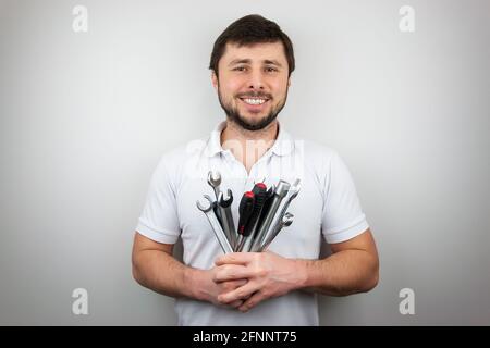 Un sourire heureux barbu dans un T-shirt blanc avec un bouquet de clés et de tournevis Banque D'Images