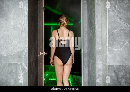 Femme marchant dans un sauna romain dans un complexe de spa en maillot de bain noir. Vue arrière. Banque D'Images