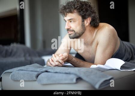 Bel homme allongé dans un salon de spa, qui attend un massage du dos et une relaxation. Le bien-être et les loisirs pour les soins de santé ensemble. Concentrez-vous sur l'homme. Regardez la caméra. Banque D'Images