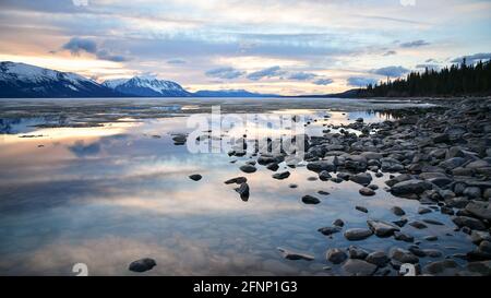 Superbe lac de printemps avec une scène de bord de lac. Glace à distance, rochers et ciel nuageux, reflet bleu dans l'eau vierge avec des montagnes enneigées. Banque D'Images