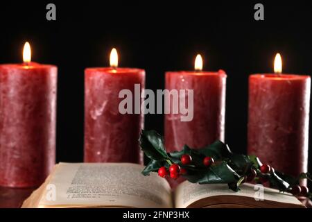 Ouvrez la bible, la branche houleuse et la couronne de l'Avent avec quatre bougies rouges brûlantes. Composition de Noël. France. Banque D'Images