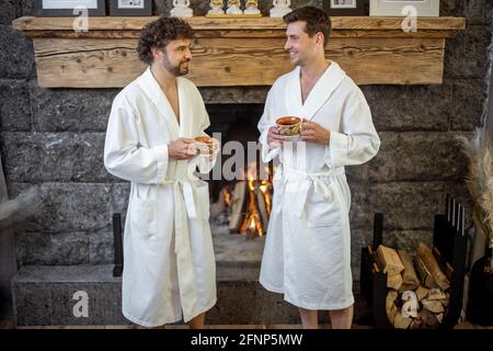 Deux personnes en peignoir se promenant près de la cheminée dans la salle de séjour de la maison de spa et de boire un thé. Concept détente et bien-être. Passer du temps ensemble. Banque D'Images