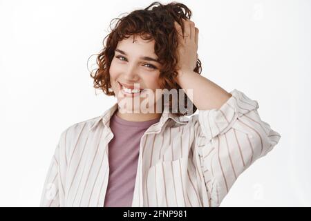 Beauté et soin de la peau. Jeune femme attrayante avec sourire heureux, cheveux bouclés courts et dents blanches, toucher la coiffure et sourire joyeux à l'appareil photo Banque D'Images