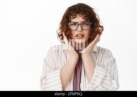 Des nouvelles terribles. Contrarié et déçu jeune femme avec des cheveux et des lunettes bouclés, frognant et regardant inquiet, étant choqué par quelque chose d'horrible Banque D'Images