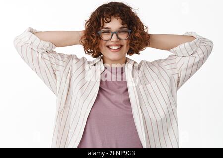 Image de la jeune femme libre et détendue dans des lunettes, tenir les mains derrière la tête de repos, avoir une pause, sourire heureux et heureux, profiter du week-end, paresseux Banque D'Images