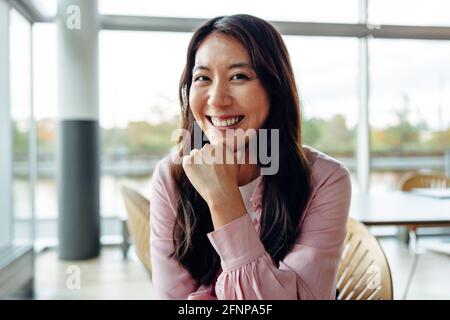 Femme entrepreneur assise au bureau. Femme souriante au bureau avec main sur le menton. Banque D'Images
