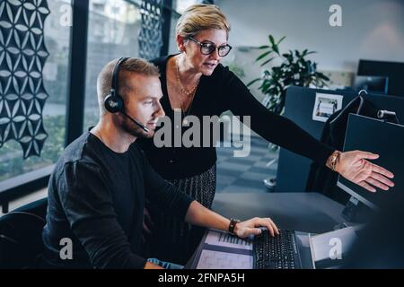 Femme professionnelle pointant sur l'écran d'ordinateur et discutant d'un problème avec un homme travaillant à son bureau. Responsable assistant l'agent du service client à la reso Banque D'Images