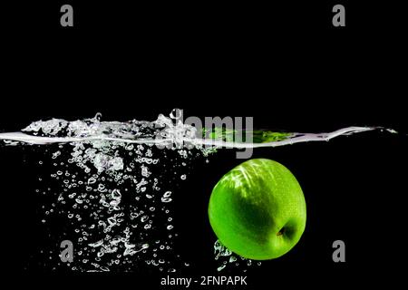 la pomme verte tombe dans l'eau sur fond noir Banque D'Images